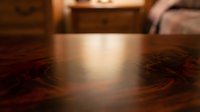 Warm sunlight streaming across polished dark wood table surface creating soft golden glow in cozy bedroom interior with furniture in background.
