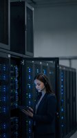 Female IT professional using tablet in modern data center with glowing blue server racks for technology and cloud computing operations.