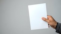 Male hand holding blank white paper sheet against neutral gray background for mockup, branding, or presentation purposes.