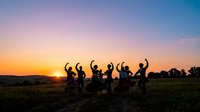 Silhouettes of diverse young adults jumping and celebrating together in rural field at golden sunset, expressing joy and freedom outdoors.