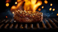 Juicy grilled beef steak with spices and herbs on barbecue grill with fire flames and smoke in dark background, close up view of premium meat cut.