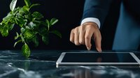 Businessman in blue suit touching tablet screen with green plant nearby, representing sustainable digital business solutions.