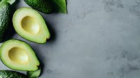 Fresh avocado halves with broccoli and green leaves on gray concrete background with copy space for healthy eating and organic food concepts.