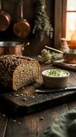 Sliced seeded bread with herb butter spread on rustic wooden board in warm kitchen setting with dried herbs and cookware for culinary content.