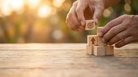 Businessman hands stacking wooden blocks with target and arrow icons representing goal achievement and strategic planning in warm sunlight.