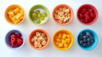 Fresh healthy snacks in colorful ceramic bowls arranged in rows on white background. Variety of fruits, berries and cereal for balanced nutrition.