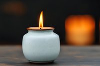 Glowing flame in white ceramic candle holder against dark background creates cozy atmosphere. Orange light illuminates minimalist composition.