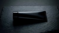 Black cosmetic tube on dark slate surface for skincare product packaging and beauty brand marketing campaigns.