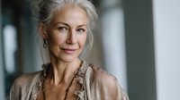 Elegant senior woman with silver hair and natural makeup smiling gently in soft light, wearing beige outfit with textured accessories for lifestyle and wellness content.