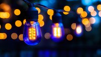 Glowing blue LED string lights with vintage-style bulbs against blurred golden bokeh background create atmospheric outdoor lighting ambiance at dusk.
