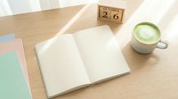 Overhead view of open blank notebook on wooden desk with matcha latte, calendar showing October 26, and pastel notebooks, suitable for stationery, productivity, and lifestyle blogging.