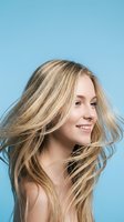 Young blonde woman with flowing hair in motion against blue background, expressing joy and freedom for beauty and lifestyle campaigns.