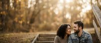Young couple sitting together on wooden steps outdoors during golden hour, enjoying intimate moment in nature with blurred forest background.