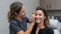 Female esthetician examining client's face during skincare consultation in modern beauty clinic, showcasing professional dermatology treatment.