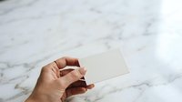 Closeup of hand holding blank white business card against marble surface for branding mockup and corporate identity design projects.