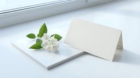 Blank greeting card with white jasmine flowers and green leaves on white surface, suitable for wedding invitations, thank you notes, and stationery design.