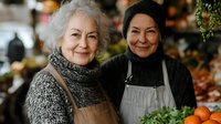 Senior women small business owners at local market stand with fresh produce, wearing aprons and displaying oranges, representing active aging and entrepreneurship.