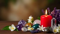 Spa wellness arrangement with red candle, healing crystals, jasmine flowers and lavender on wooden surface for relaxation and meditation practices.