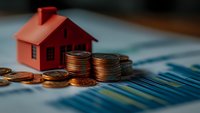Red miniature house model with stacked coins on financial chart background, representing real estate investment, mortgage rates and property market analysis.