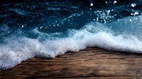 Ocean wave with white foam crashing onto wooden deck or pier, creating dramatic contrast between dark wood texture and blue water, captured in close-up perspective.