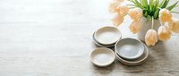 Ceramic dishes and pastel tulips arranged on a rustic wooden table, soft spring styling for home decor, food photography, or lifestyle blog.