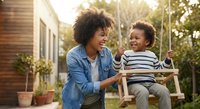 African American mother and son enjoying quality time together on wooden swing in sunny backyard garden setting for family lifestyle content.