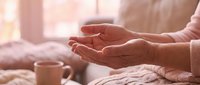 Elderly woman's wrinkled hands in prayer position during peaceful morning meditation with warm sunlight streaming through window creating serene atmosphere.