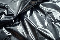 Crumpled black plastic garbage bag surface with shiny reflective folds and wrinkles creating abstract texture pattern. Suitable for environmental or waste concepts.