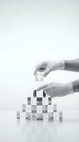 Hands in white gloves placing transparent building blocks in pyramid formation, symbolizing construction, growth, and business development strategy.