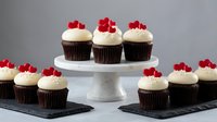 Chocolate cupcakes with vanilla frosting topped with red heart candies on white cake stand and slate boards for Valentine's Day celebration dessert.