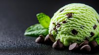 Mint chocolate chip ice cream scoop with fresh mint leaves and chocolate chips on dark background, creamy dessert with vibrant green color and rich texture.