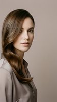 Young Caucasian woman with long brown hair wearing beige shirt on neutral background for beauty and fashion concepts.