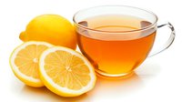 Fresh cut lemons and glass cup of hot tea on white background, bright yellow citrus fruit slices next to transparent teacup for healthy drink concept.