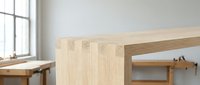 Modern minimalist wooden dining table in bright contemporary interior with natural light from large windows creating clean Scandinavian home design atmosphere.