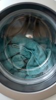 Teal towel inside washing machine drum during laundry cycle for household cleaning and domestic chores.