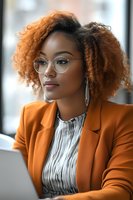 Professional African American businesswoman with curly hair and glasses working on laptop in modern office environment for corporate presentations.