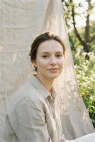 Young Caucasian woman in linen shirt smiling outdoors in natural sunlight with green foliage background for lifestyle and wellness content.
