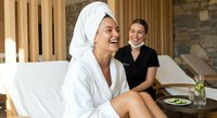 Two young Caucasian women relaxing at luxury spa resort, one in white bathrobe with towel on head, enjoying wellness treatment and healthy lifestyle.