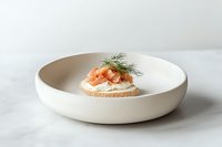 Open sandwich with smoked salmon, cream cheese and fresh dill on round bread slice, served in minimalist white ceramic plate against marble background.