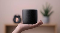 Smart speaker floating on female hand against blurred home interior background with decorative elements and soft lighting creates modern lifestyle atmosphere.