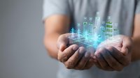 Hands holding glowing holographic cityscape with digital buildings and technology icons, representing smart city development, urban innovation, and future infrastructure planning.