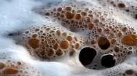 Macro shot of coffee foam with bubbles creating abstract texture pattern. Dark roasted coffee crema with tiny air bubbles forming artistic surface detail.