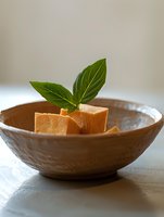 Fresh cantaloupe melon cubes garnished with green basil leaves served in rustic ceramic bowl on light background, minimalist food styling for healthy eating.