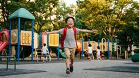 Young Asian boy in striped shirt running joyfully at colorful playground with climbing equipment and slides in sunny park setting for active childhood recreation.
