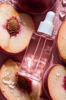 Fresh peach serum dropper bottle with water drops and sliced nectarines on pink background, natural skincare and beauty product photography.