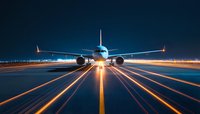 Commercial passenger aircraft on runway at night with dramatic lighting, glowing navigation lights and illuminated markings creating leading lines to horizon.