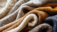 Cozy knitted sweaters in neutral earth tones folded in layers creating soft textured waves, perfect for fashion, lifestyle and autumn seasonal content marketing and design projects.