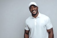 Happy African American man in white polo shirt and cap smiling at camera against gray background for lifestyle and fashion content.