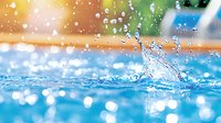 Fresh water splash with sunlit droplets creating dynamic motion against blurred summer pool background with bokeh lights and rainbow color reflections.