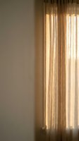 Sunlight filters through sheer linen curtains in warm golden tones, creating soft shadows on a neutral wall. Ideal for home decor, interior design, and lifestyle content.